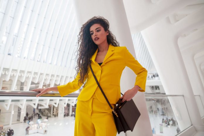 Woman carrying a chestnut brown recycled leather handbag in NYC, styled with a yellow suit at Oculus